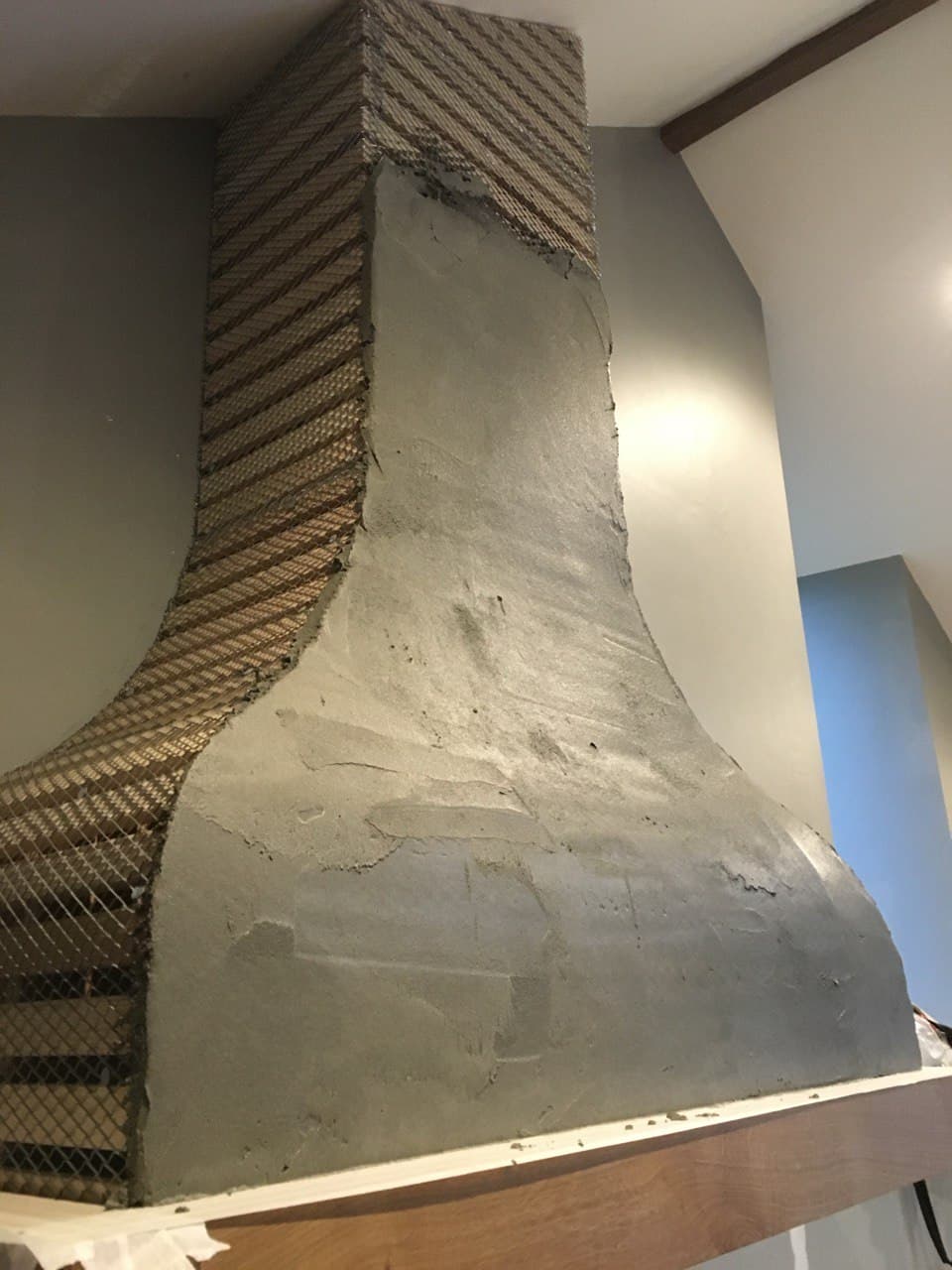 Base render coat being applied over mesh framework on bespoke chimney hood showing construction process