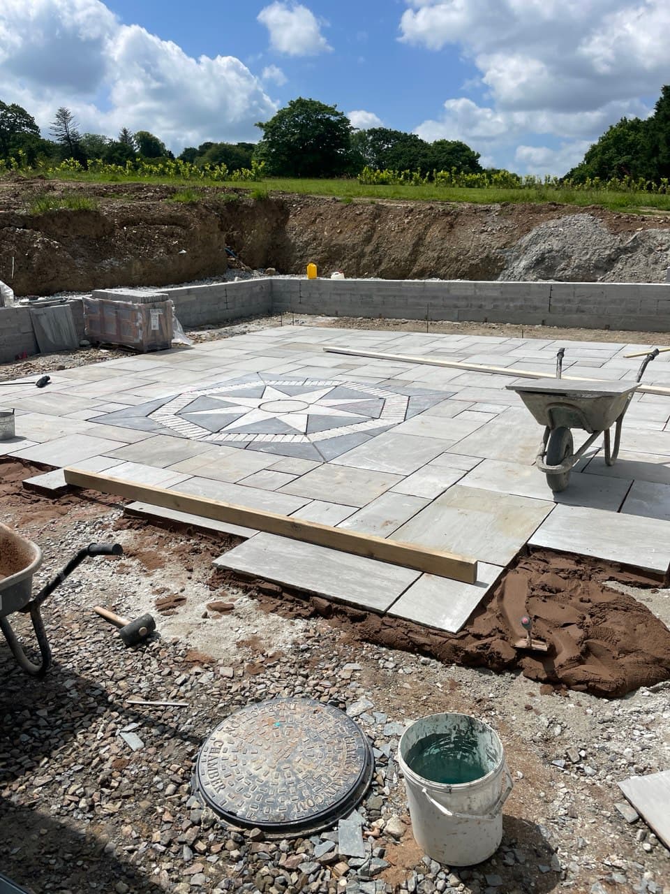 Near-complete natural stone patio with compass rose centrepiece and blockwork retaining walls at Thornbury Devon new build