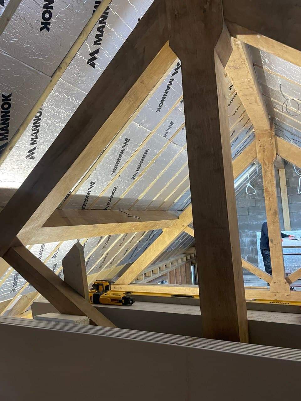 Close-up of oak timber king-post trusses with insulation and plasterboard being installed during new build interior fit-out