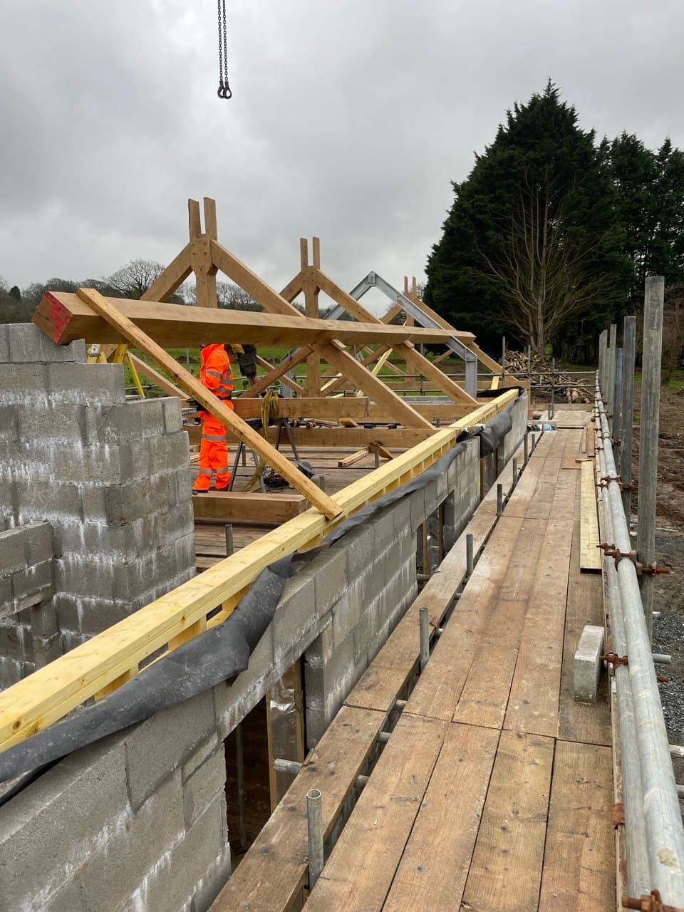 Construction worker in high-visibility gear securing oak roof trusses on scaffolding during new build project