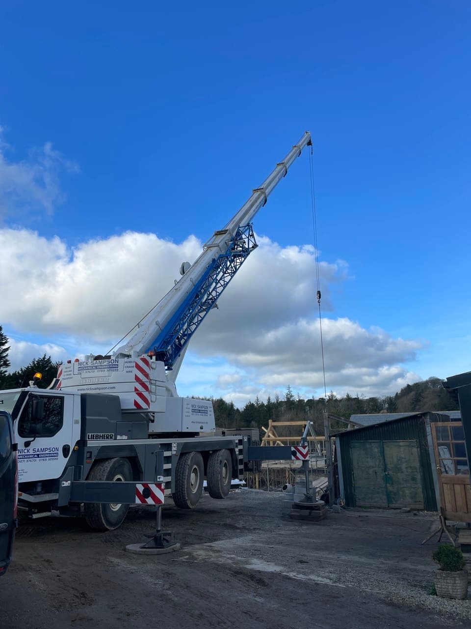 Liebherr mobile crane on stabiliser legs at Thornbury Devon new build construction site ready to lift oak roof trusses