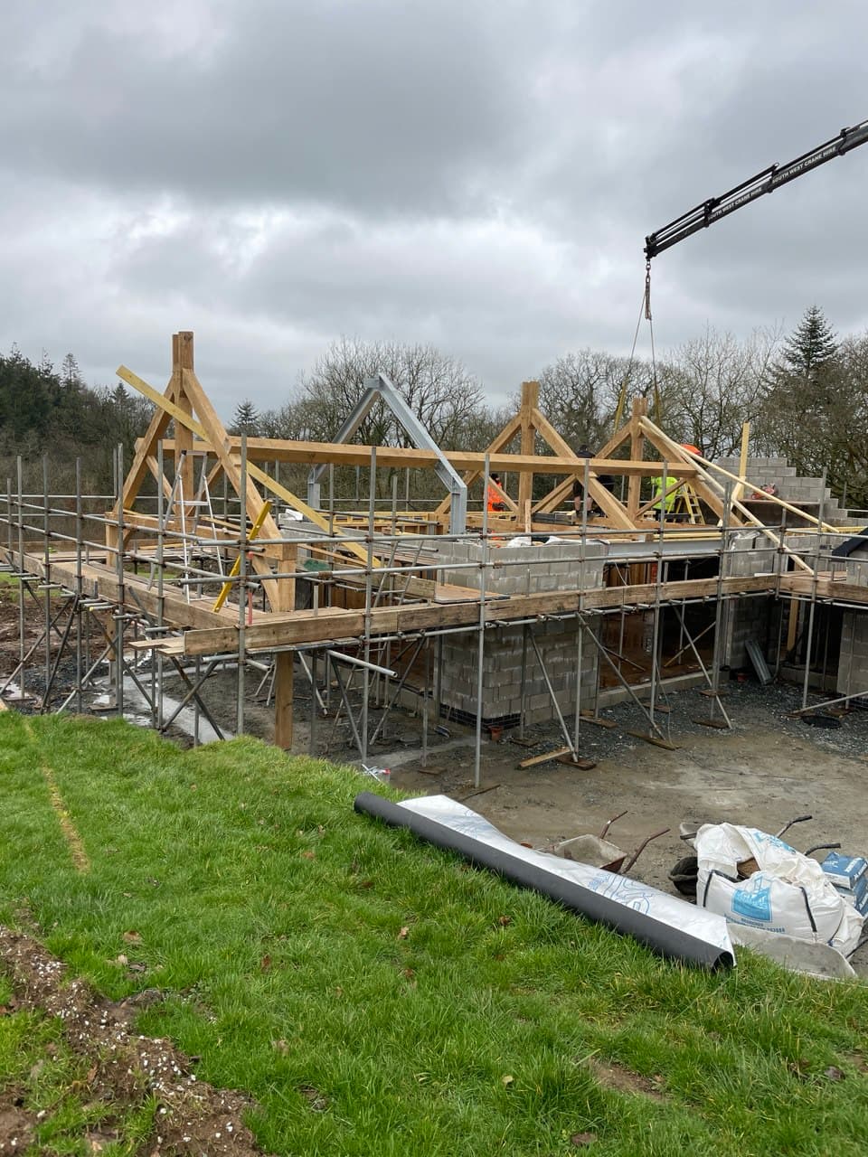 Wide view of new build construction site showing blockwork walls and crane-lifted roof trusses with scaffolding