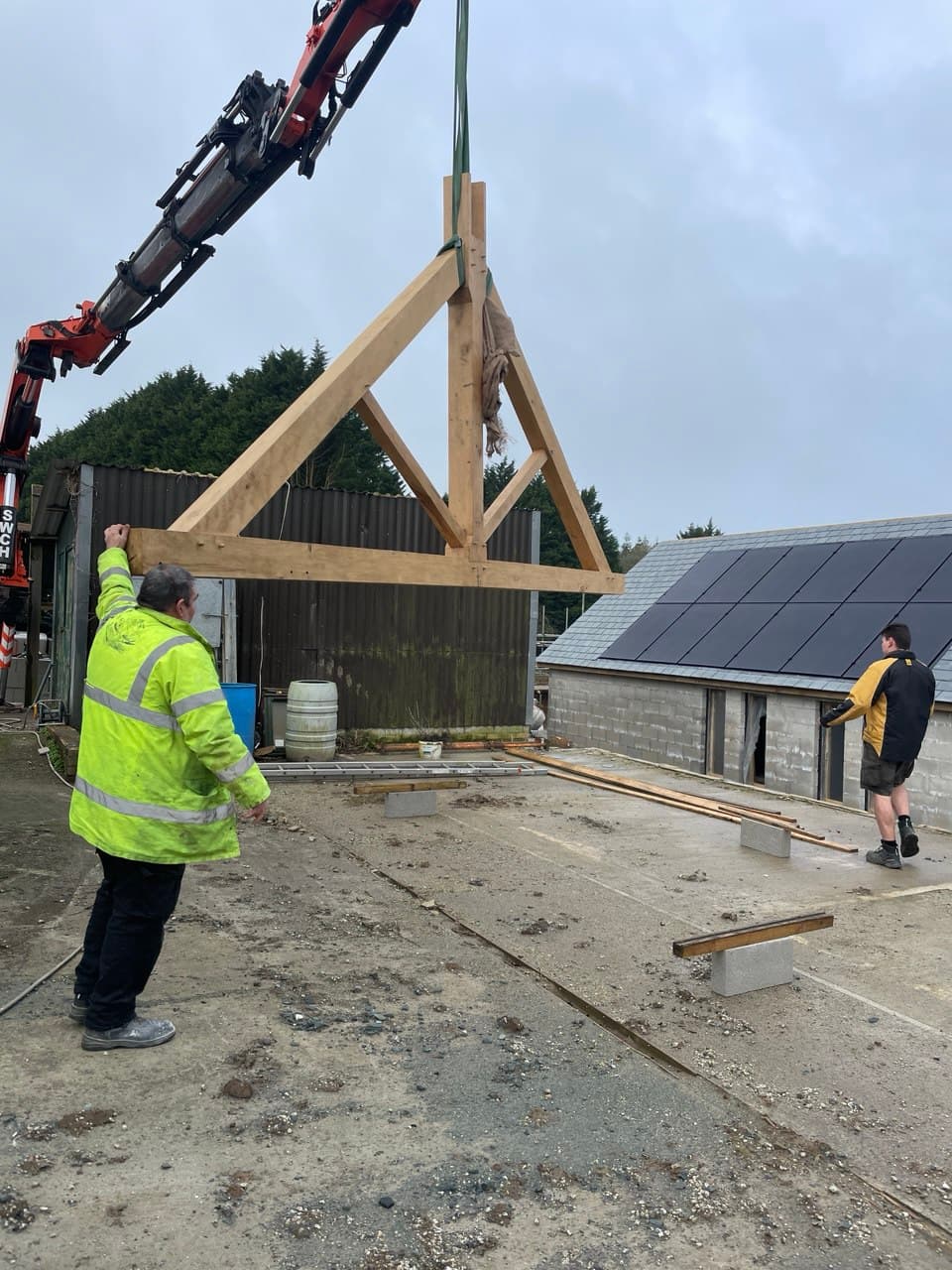 Workers guiding a large oak roof truss being lowered by crane at Thornbury Devon construction site