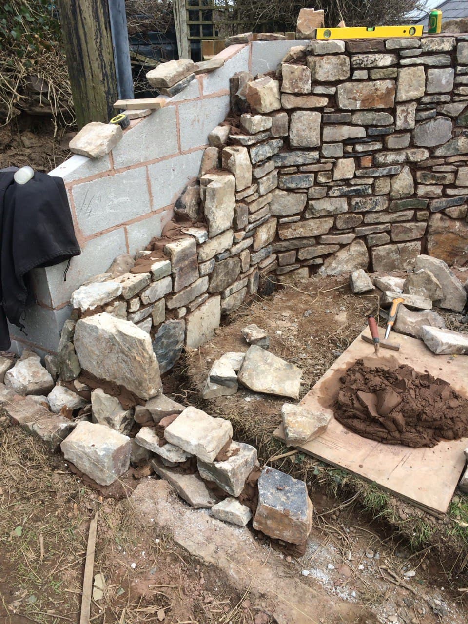 Traditional stone wall under construction showing blockwork core faced with natural stone and lime mortar